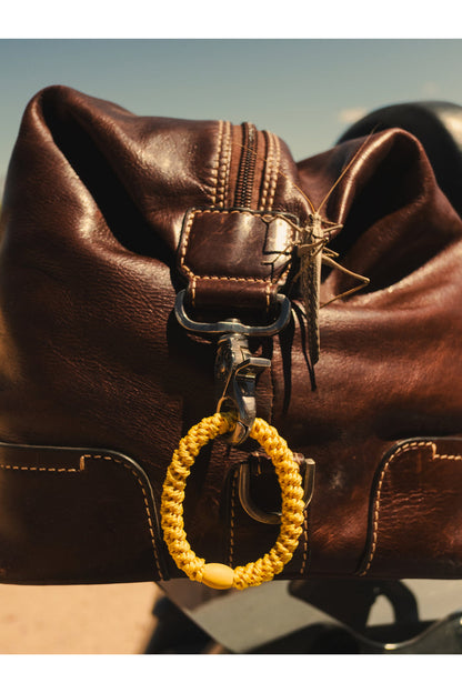 KKNEKKI Sun yellow braided elastic hair tie hanging on a brown leather bag with metal clasp, by KKNEKKI. Shop KKNEKKI at Dotique.